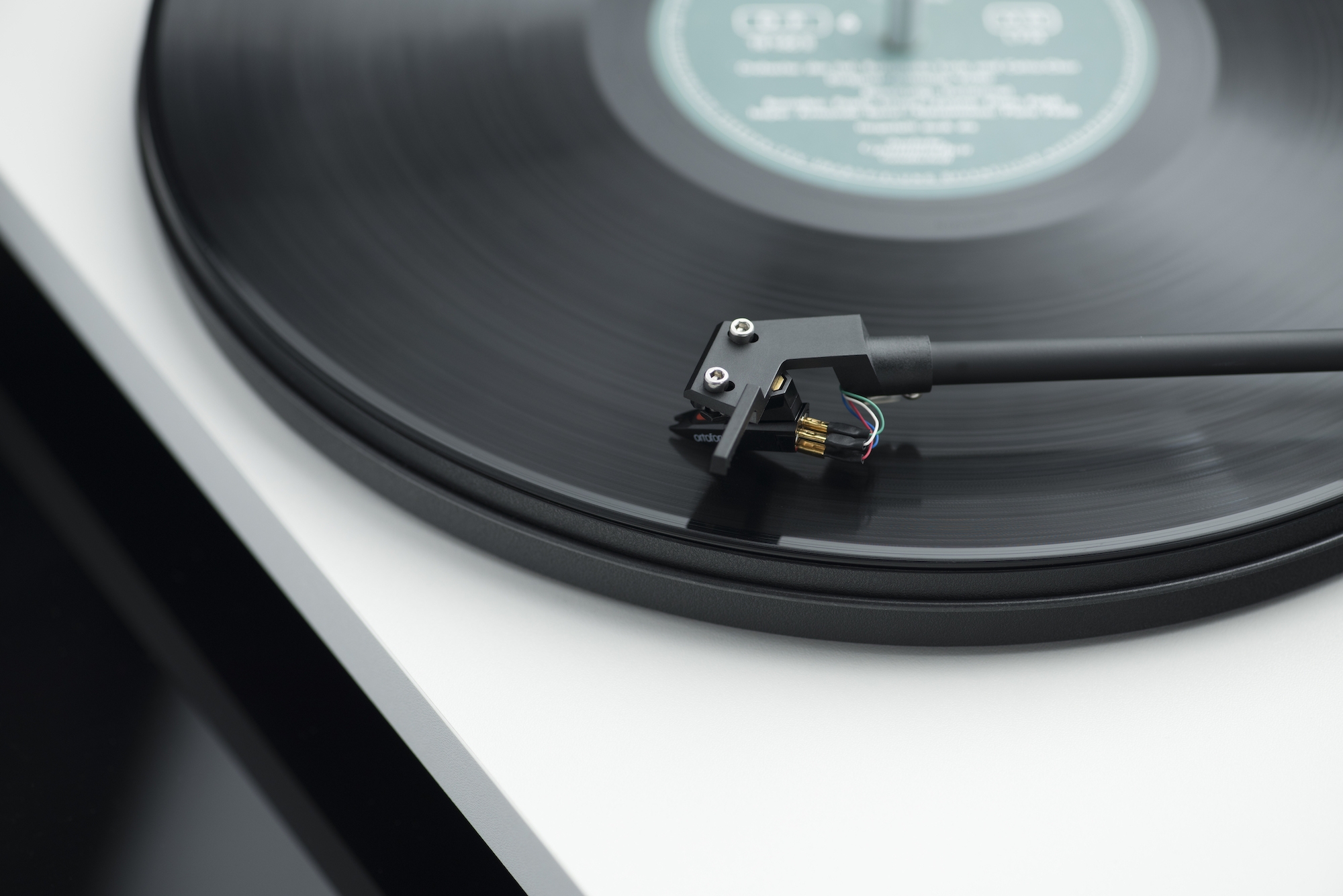 Pro-Ject Primary E Turntable With Om Cartridge Close-up of a spinning vinyl record on a turntable, showing the tonearm cartridge and color-coded wires.