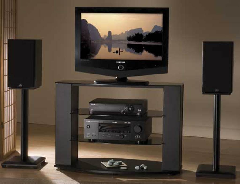 Sanus Nf24 24&Quot; Natural Series Wood Pillar Bookshelf Speaker Stands Samsung flat-screen tv on a black glass media stand with two tall speakers and stacked av components.