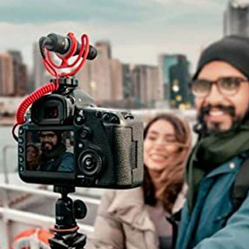 Rode Videomicro Dslr camera on a small tripod with red coiled cable, city skyline background and smiling couple.
