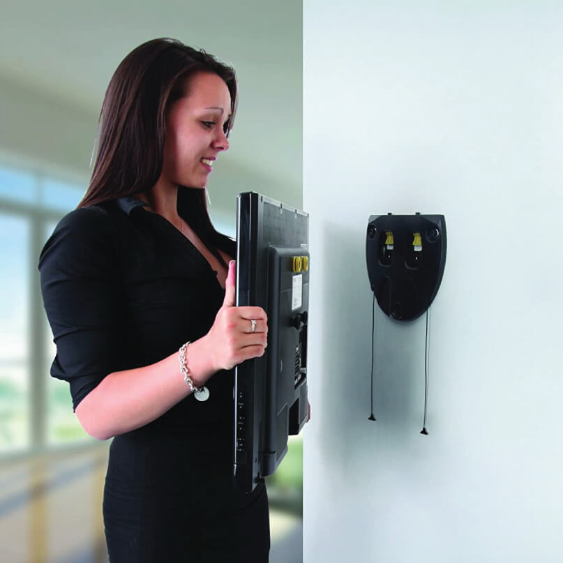 Avf Unimax Any Wall Flat To Wall Tv Mount Woman in black shirt holding a flat-screen monitor near a wall-mounted device with yellow connectors.