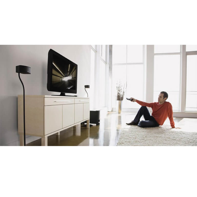 Bose Ufs-20 Series Ii Universal Floorstands-Black/White Flat-screen tv on a light wood media console in a bright living room; person in red sweater holds a remote.
