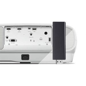 Rear view of the Epson EH-TW7100 4K PRO-UHD Projector showing ports including HDMI and USB, with a black rectangular streaming stick plugged into the right side.