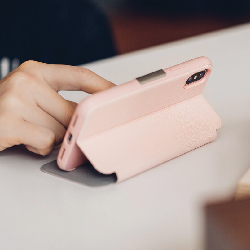 Moshi Sensecover For Iphone X/Xs - Black Pink phone case with a built-in stand propping a smartphone on a desk.