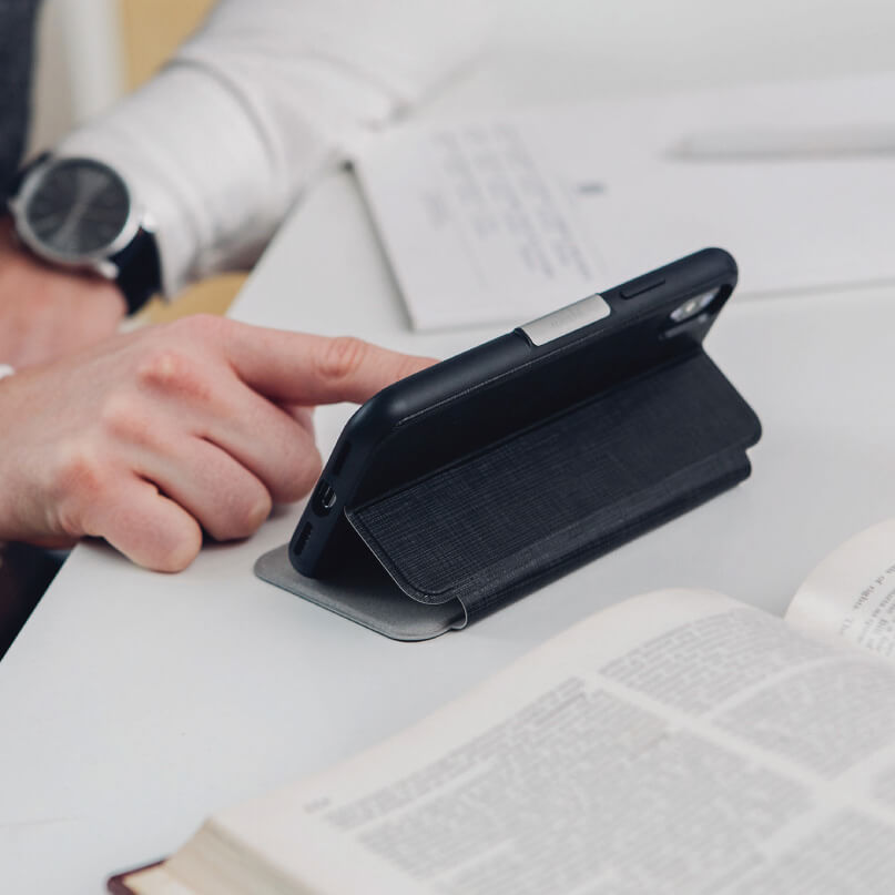 Moshi Sensecover For Iphone X/Xs - Black Smartphone in a black folio case with built-in stand on a desk beside an open book.