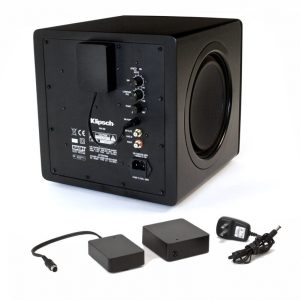 Klipsch powered subwoofer with control panel, rear inputs and power adapters in a black cube enclosure.