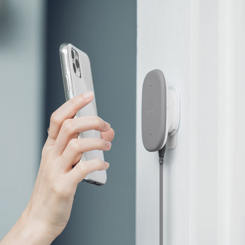 Moshi Snapto Magnetic Wireless Charger W/ Wall Mount Kit (Grey) Silver iphone with a triple-camera setup held near a gray wall-mounted wireless charger.
