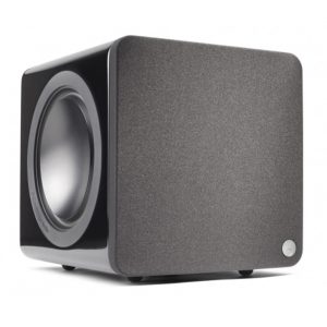 Black subwoofer with fabric front panel, large circular woofer on left, and small round badge on bottom-right.