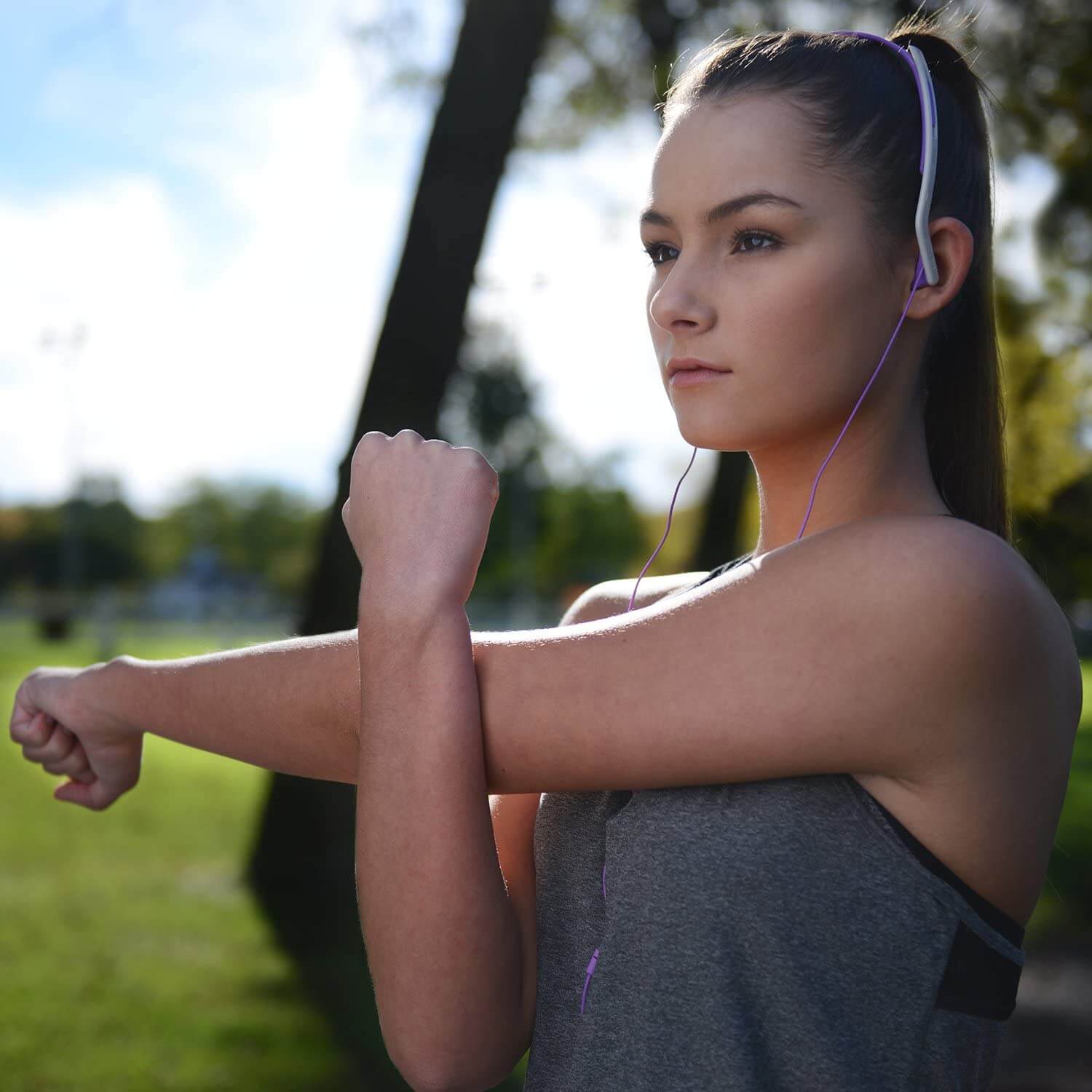 Koss Kph14 On Ear Headphones Woman wearing purple wired earphones outdoors, gray athletic top, stretching her arms.
