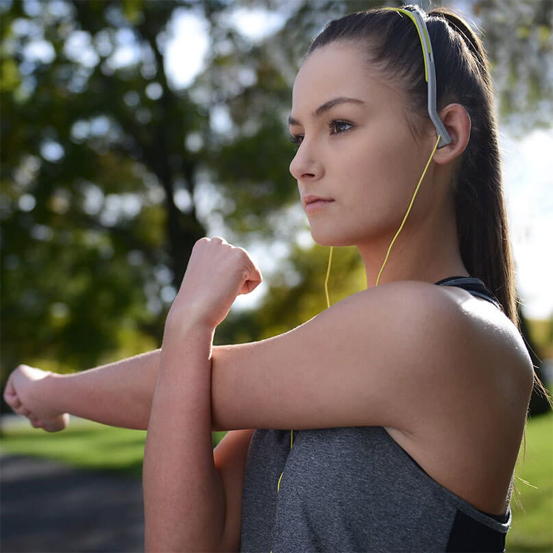 Koss Kph14 On Ear Headphones Woman wearing neon yellow wired in-ear headphones while stretching outdoors.