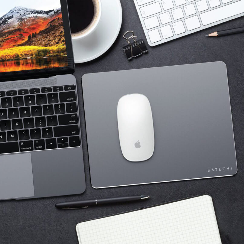 Satechi Aluminium Mouse Pad Apple macbook pro laptop with white magic mouse on a satechi desk mat beside a white keyboard and coffee cup.