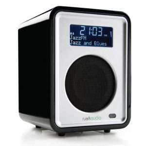 Ruark Audio compact digital radio with blue LCD display, silver front panel, circular speaker grille, black enclosure.