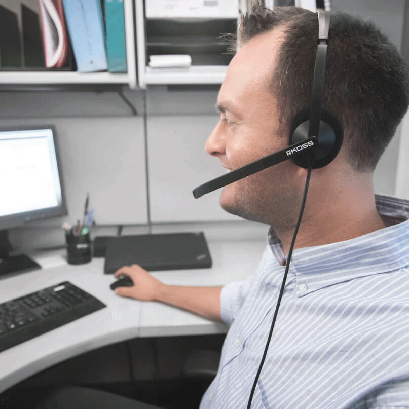 Koss Cs200-Usb Headphones Person wearing a black koss headset with boom microphone at a computer desk.