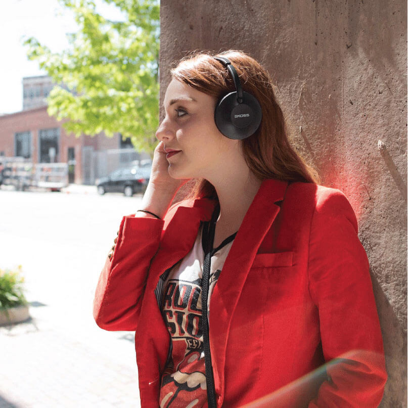 Koss Kph7 Wireless Headphones Woman wearing boss over-ear headphones with padded cups outdoors, red jacket.