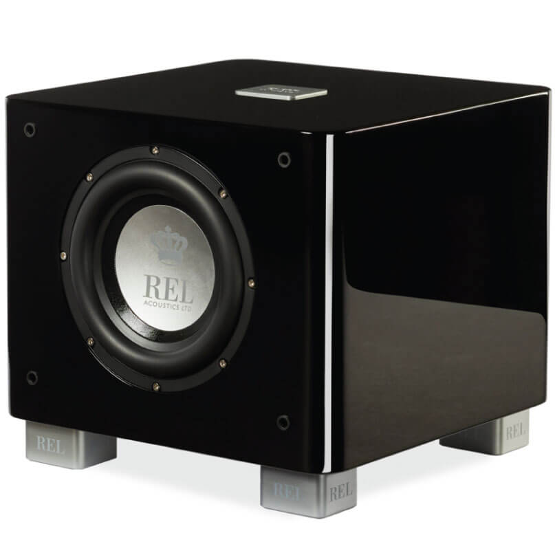 Rel Serie T/7X Rel acoustics subwoofer in a glossy black cabinet with a front-facing 12-inch driver and silver logo, supported by silver feet.