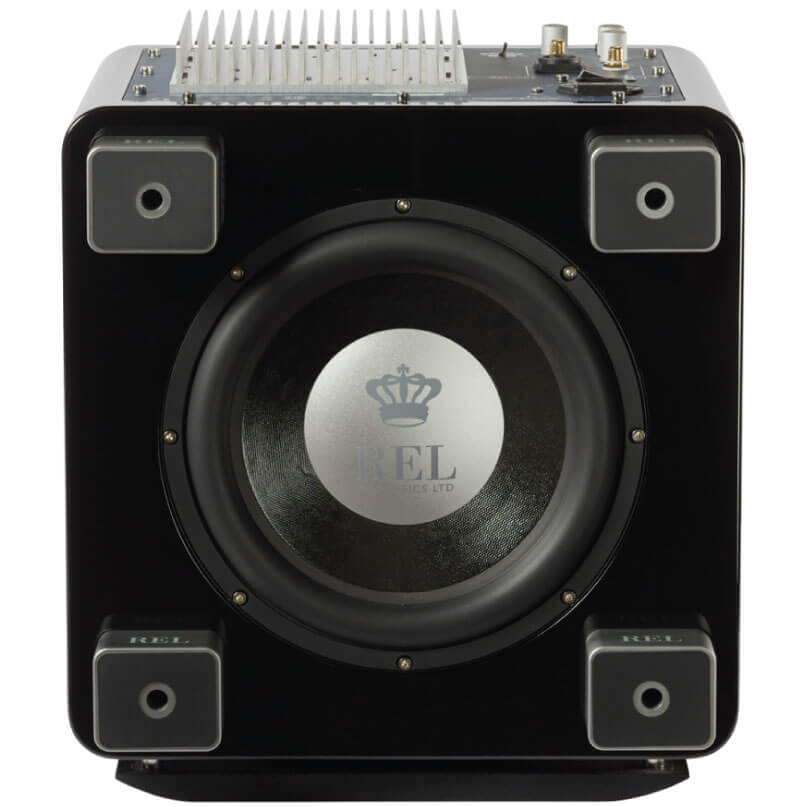 Rel Serie T/7X Rel subwoofer with black gloss cabinet, large front woofer, silver logo disk, four metal feet, and top heatsink with connectors.