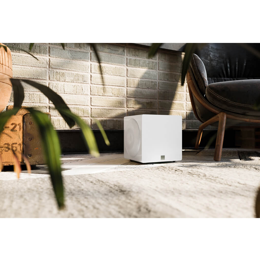 Svs 3000 Micro Subwoofer White cube-shaped wireless speaker with circular side grille sits on a wooden deck beside a chair.