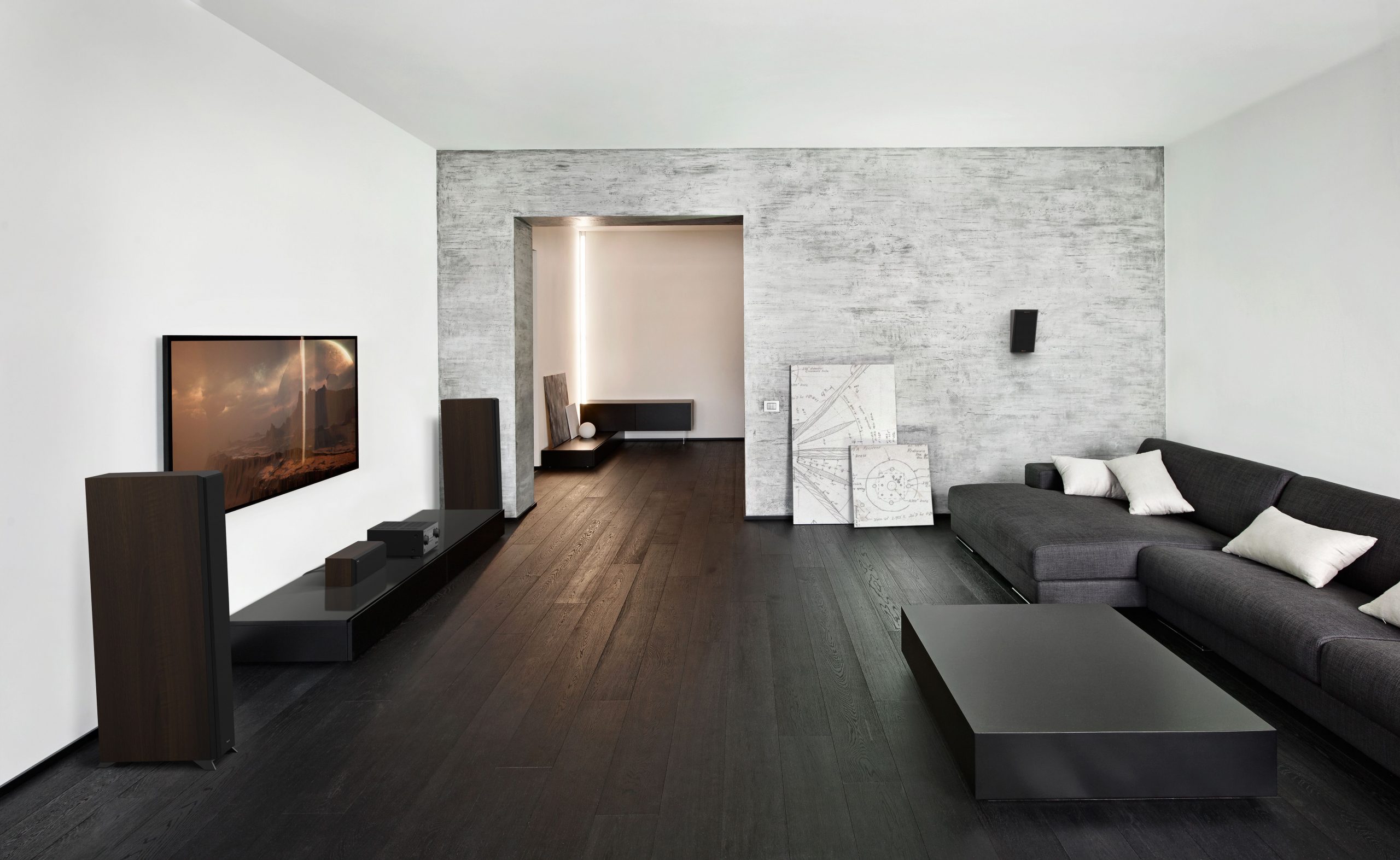 Klipsch Rp-6000F Ii Modern living room with dark wood floor, grey textured wall, large tv on black console, black speakers, and sectional sofa.