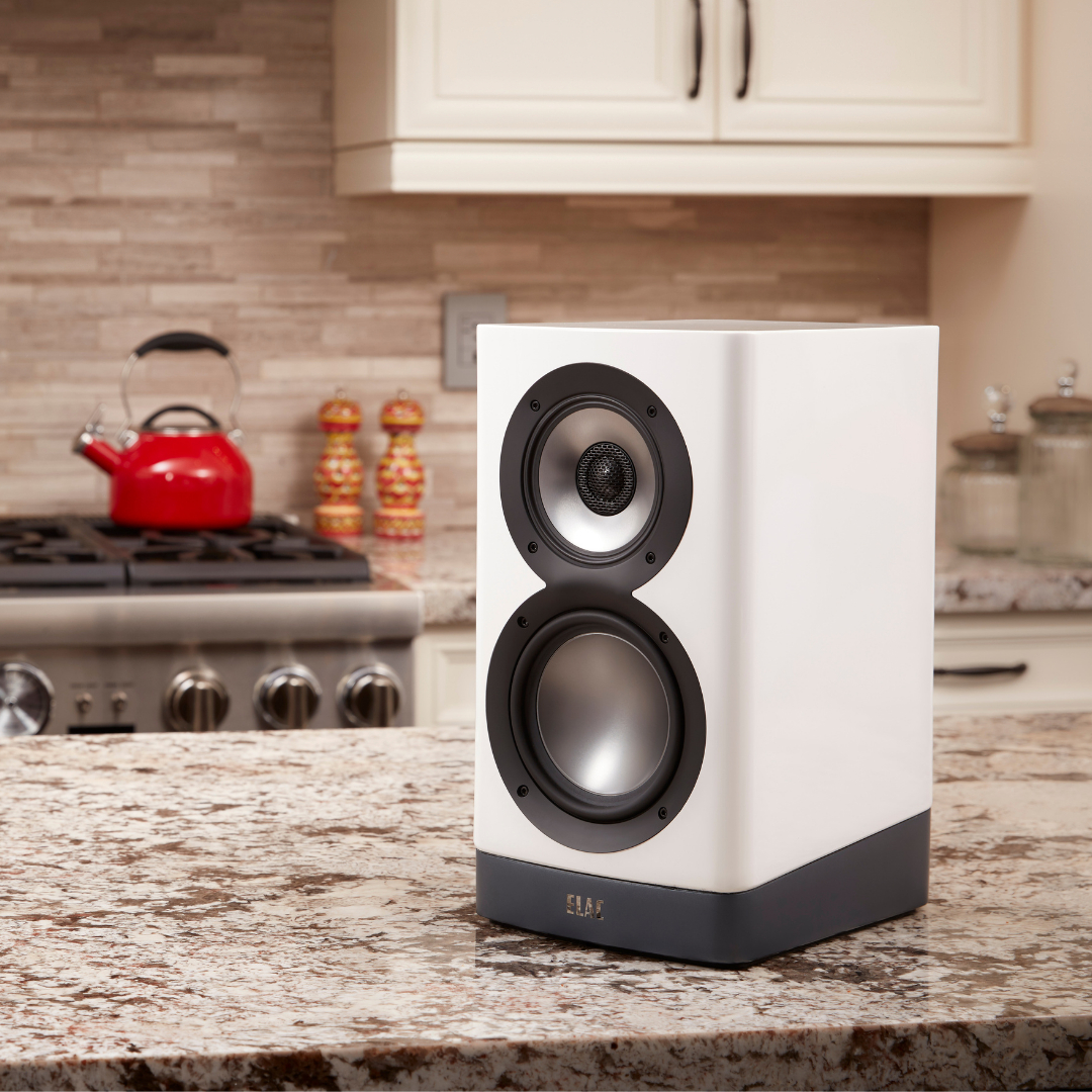 Elac Navis Arb-51 Bookshelf Speakers Elac white bookshelf speaker with a small top driver and larger bottom woofer on a kitchen counter.
