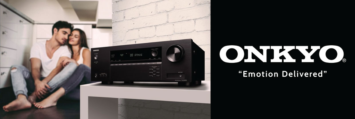 Onkyo black av receiver with display and large front knob on a white table, blurred couple in the background