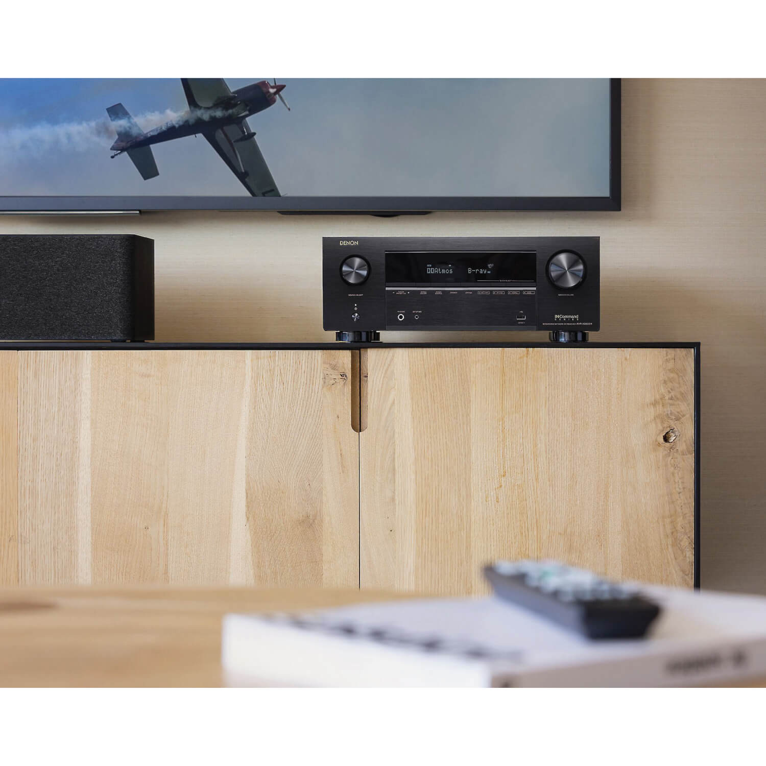 Denon Avr-X2800H 7.2Ch 8K Av Receiver Denon av receiver with black metal finish, two large knobs on the sides, digital display, placed on a wooden cabinet.