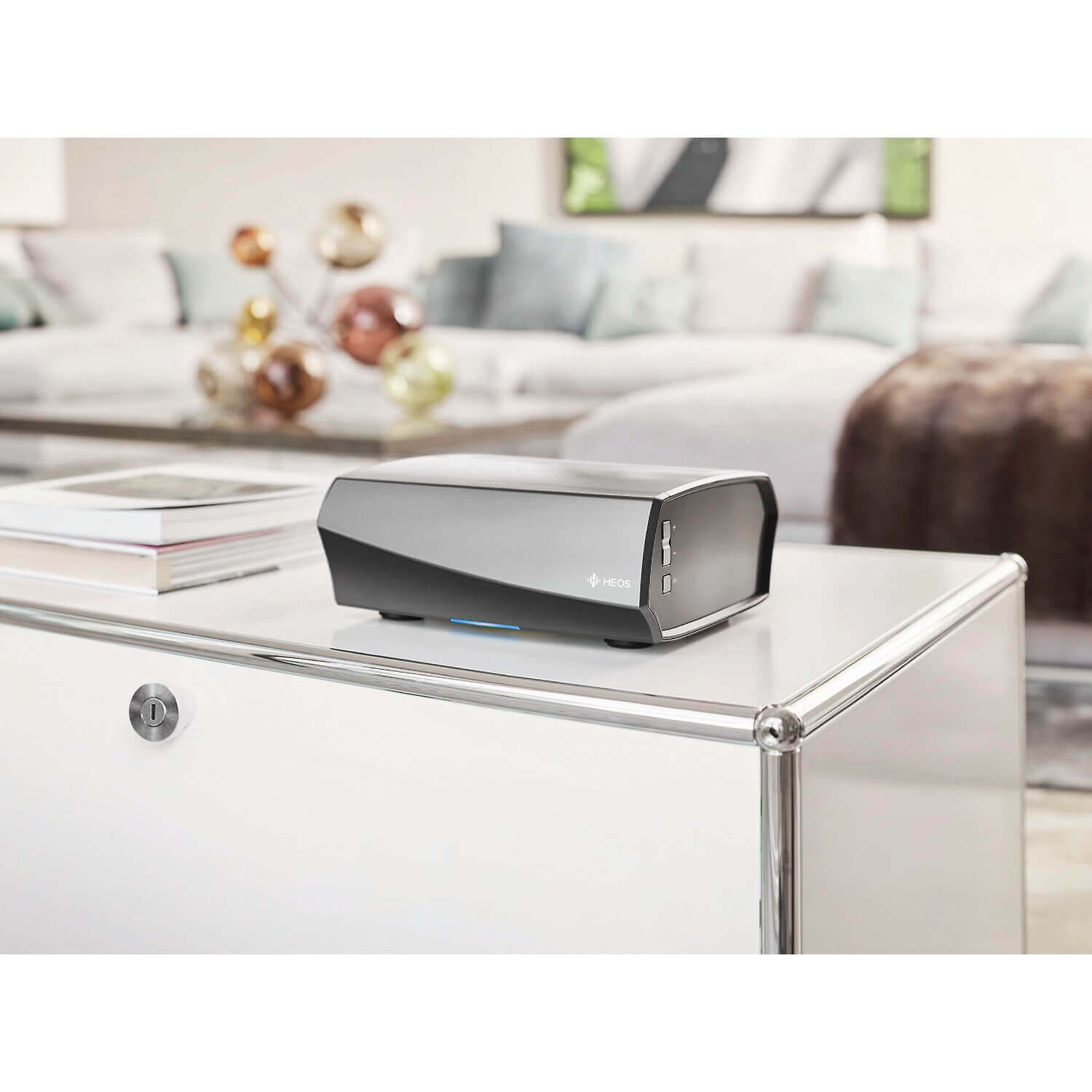 Denon Heos Amp Hs2 Heos wireless music player with a curved dark gray body and blue led light on a glass coffee table.