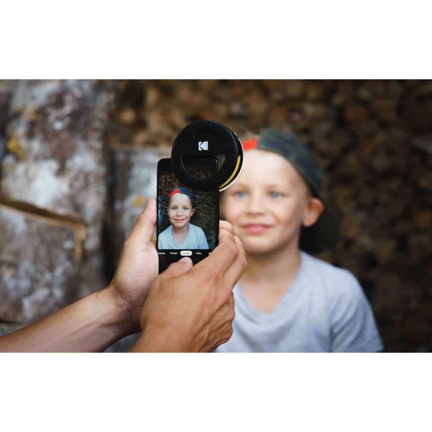 Kodak Smartphone Portrait Light Smartphone with circular lens attachment mounted above the camera, showing a portrait of a smiling girl on the screen.