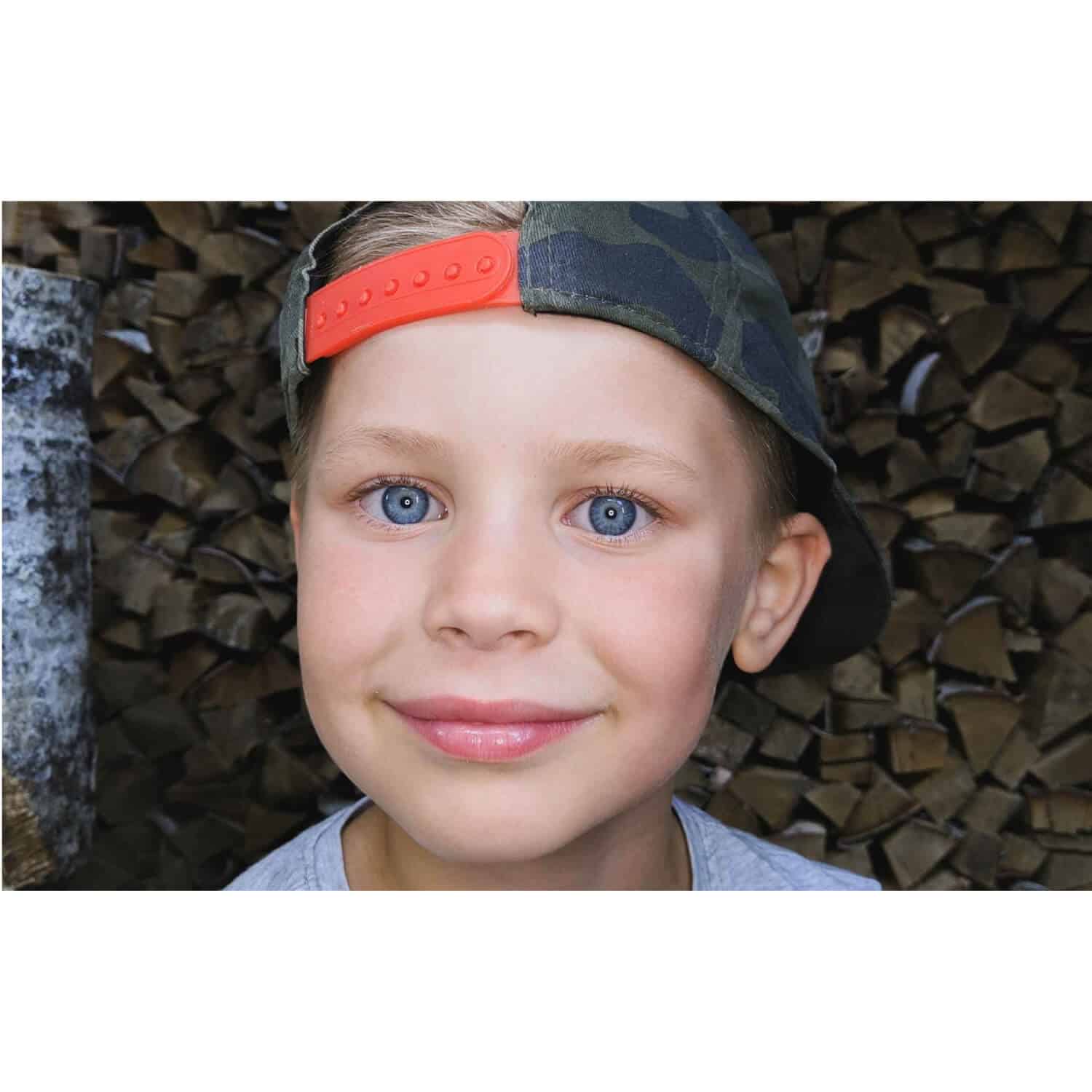 Kodak Smartphone Portrait Light Close-up of a child wearing a camouflage baseball cap with an orange snapback strap.
