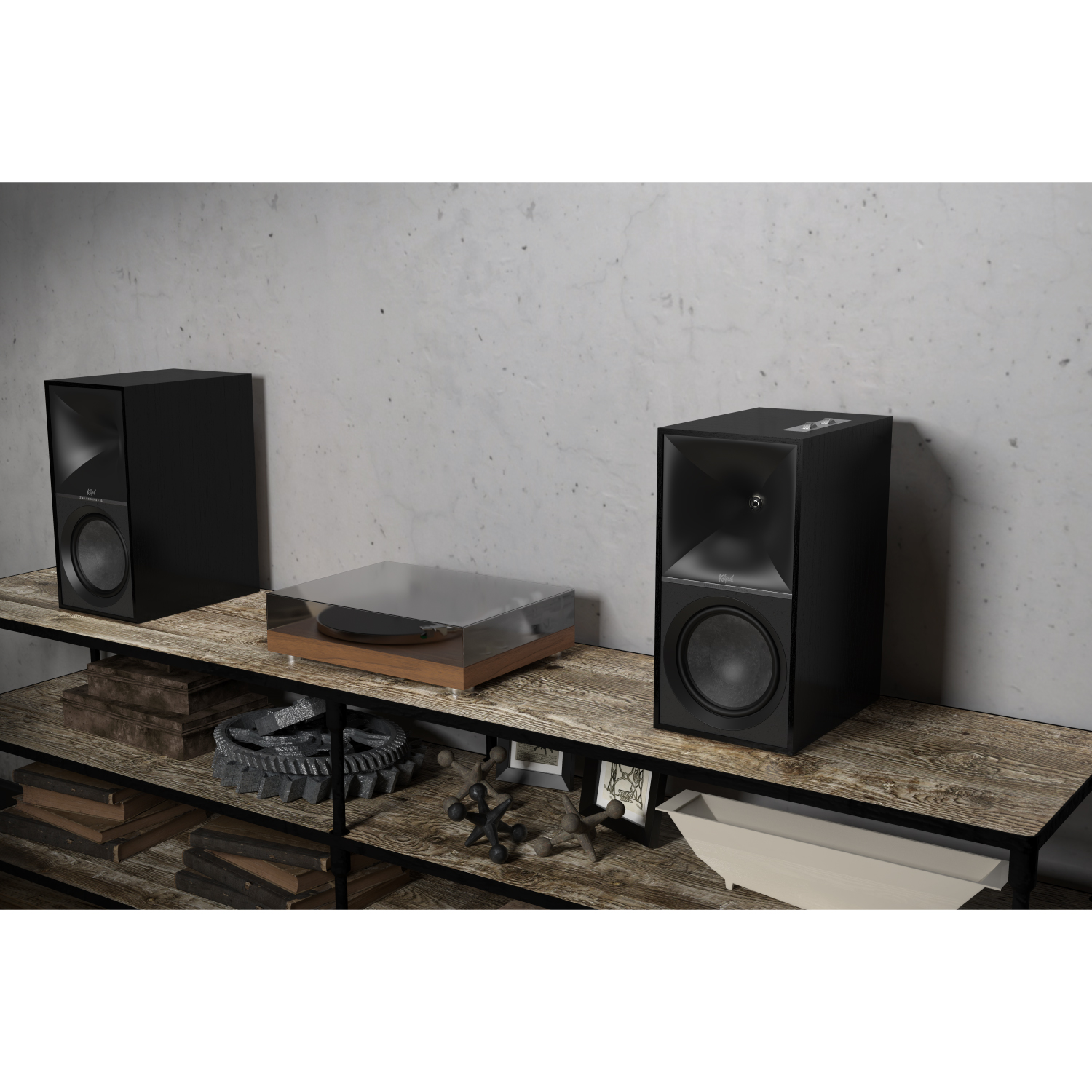 Klipsch The Nines Pair of black bookshelf speakers with a glass-topped turntable on a weathered wooden shelf against a concrete wall.