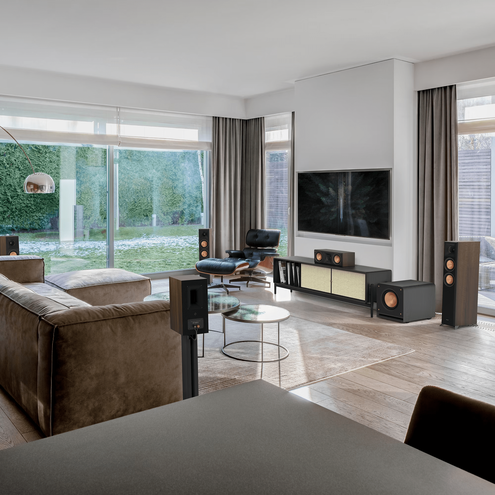 Klipsch Rp-1200Sw Modern living room with wall-mounted flat-screen tv, floor-standing speakers, glass coffee table, and brown sectional sofa.