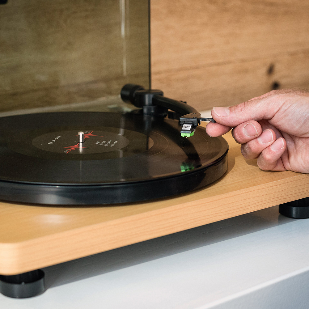 Lenco Turntable With Mmc Cartridge - Wood Turntable with raised dust cover playing vinyl record, hand adjusting tonearm and cartridge.