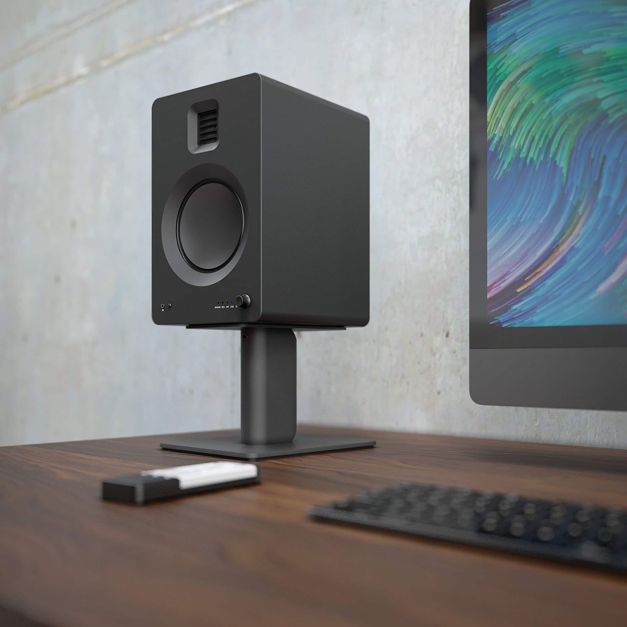Kanto Tuk 260W Powered Bookshelf Speakers With Headphone Out, Usb Input, Dedicated Phono Pre-Amp, Bluetooth - Pair, Matte Black Black studio monitor speaker with a circular driver and vent on top, mounted on a stand beside a colorful monitor.