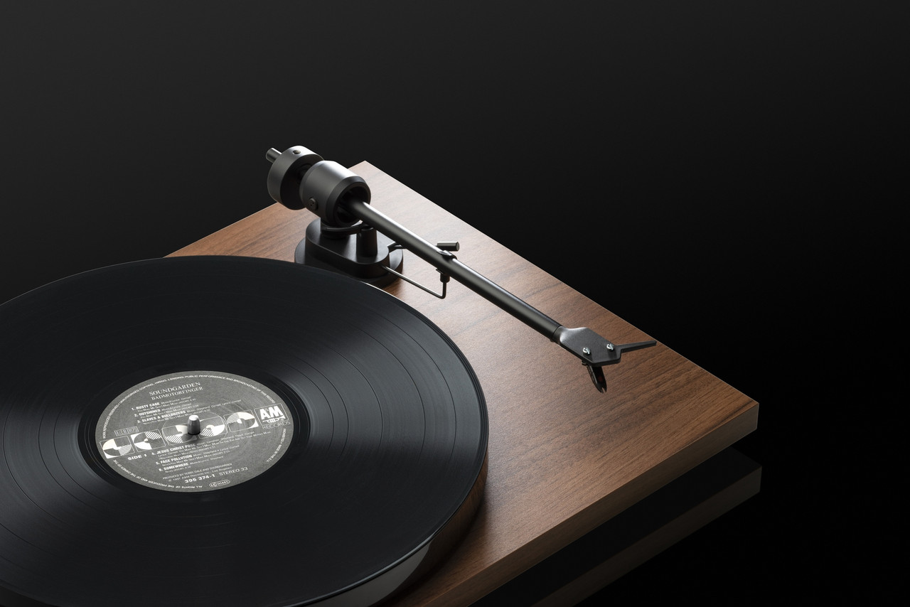 Pro-Ject E1 Phono Turntable With Ortofon Om 5E Cartridge Turntable on a wooden plinth with a black vinyl record and metal tonearm.