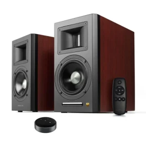 Pair of dark wood bookshelf speakers with front drivers and rectangular port, plus remote control and a circular streaming device.