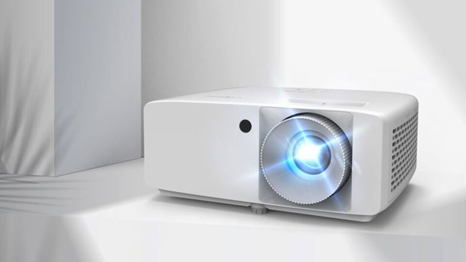Optoma Zw350E White compact projector with a blue-lit lens on the right and a vented side, resting on a white surface.