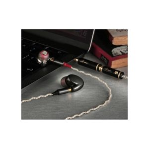 High-end in-ear monitors with a twisted white cable and gold-plated connectors, resting beside a laptop and books.