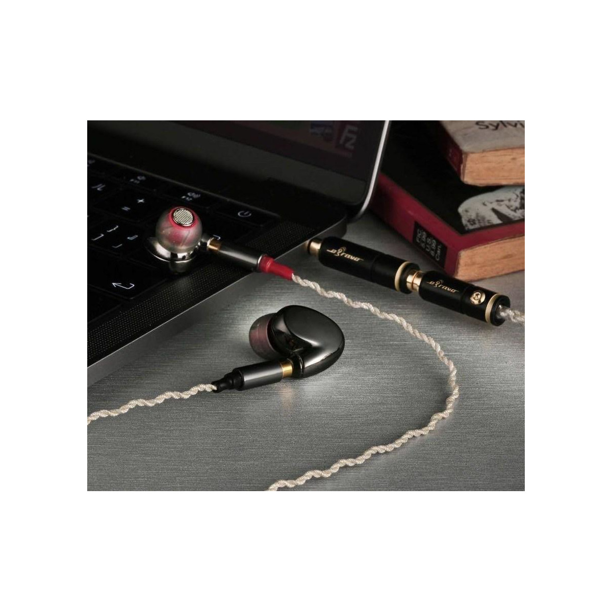 Obravo Cupid Prime High-end in-ear monitors with a twisted white cable and gold-plated connectors, resting beside a laptop and books.