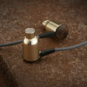 Two gold-plated microphone capsules with metal mesh tops connected by a braided cable on a brown surface.
