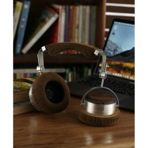 Brown suede padded over-ear headphones with a silver metal frame on a wooden desk beside a laptop.