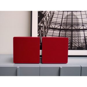 Two red square speakers with fabric fronts sit on a gray cabinet.