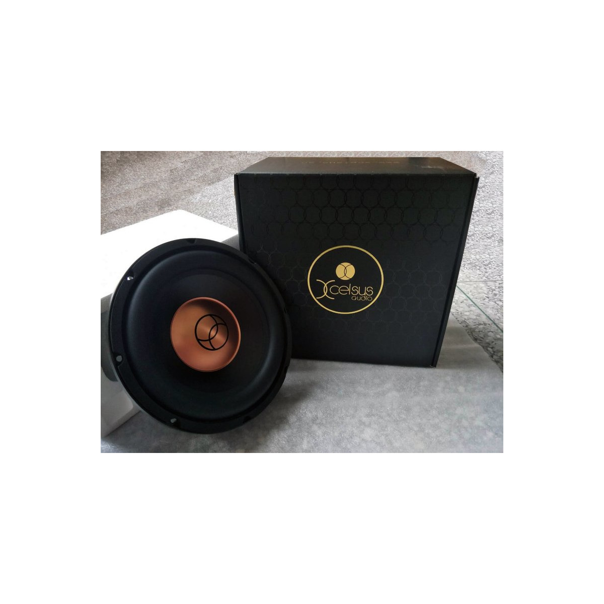 Xcelsus Audio Xxs10 Xcelus audio subwoofer with copper dust cap and black cone beside a black box featuring a gold logo