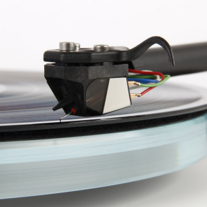 Turntable tonearm with cartridge and stylus on a spinning vinyl record, black head shell and multicolor wires visible.