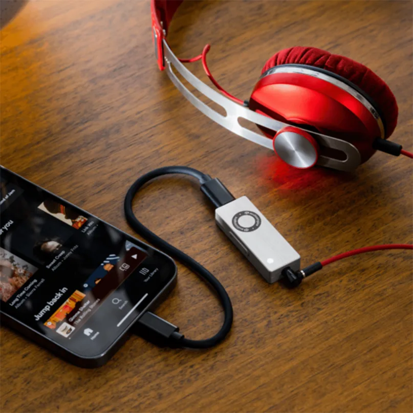 Audioengine Dac3 Portable Headphone Amplifier &Amp; Dac Red over-ear headphones connected to a portable usb dac/amp and a smartphone on a wooden table.