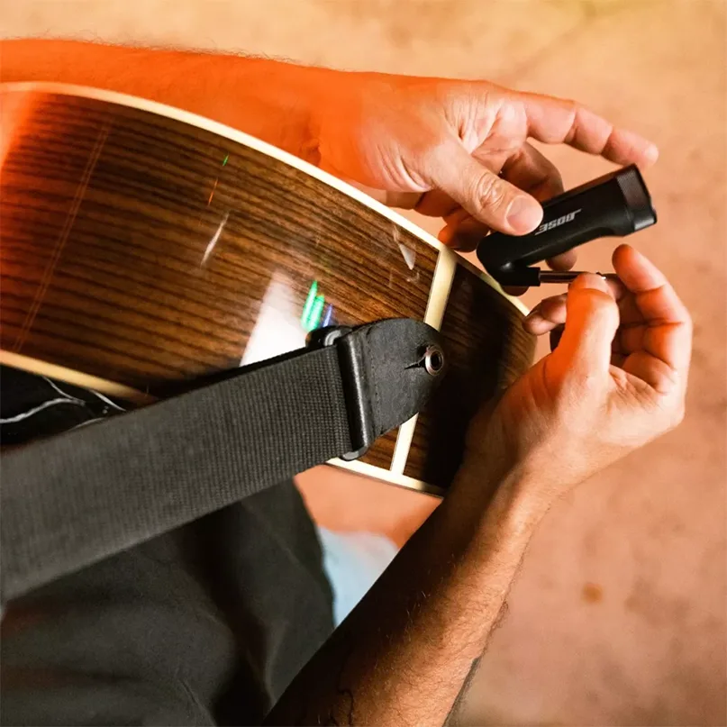 Bose Wireless Instrument Transmitter Person installing a small black clip-on guitar pickup on an acoustic guitar with a strap.