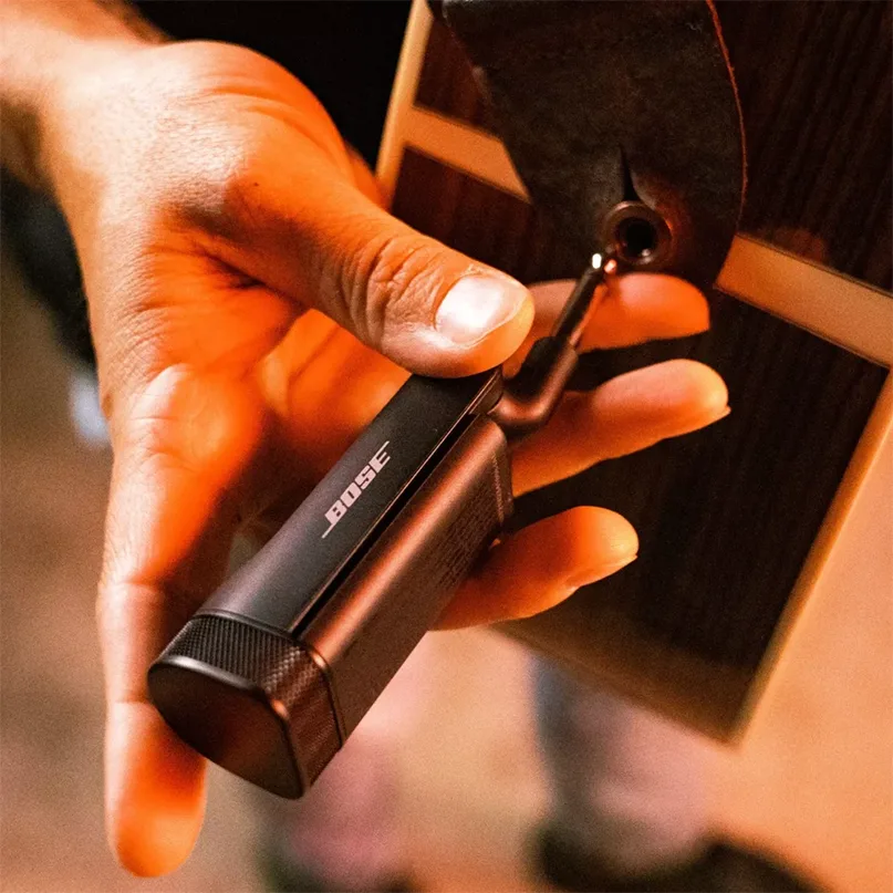 Bose Wireless Instrument Transmitter Bose clip-on guitar pickup with inline preamp, being attached to an acoustic guitar, black rectangular module and cable.