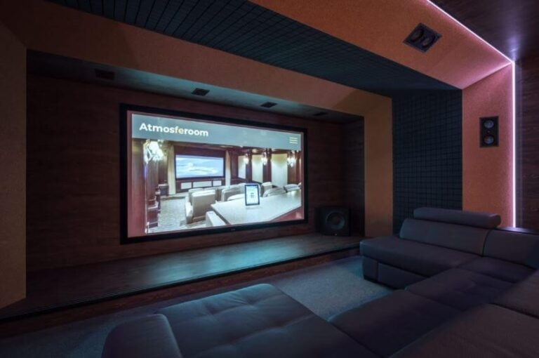 Tdg Audio Iwlcr-66V2 Dual 6.5” 3-Way In-Wall Lcr Speaker Home theater with a large screen and gray sectional seating under pink ambient lighting.