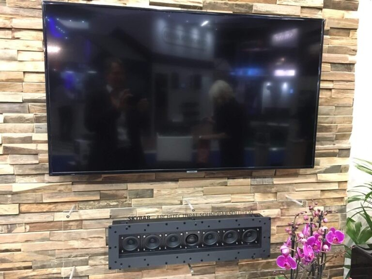 Tdg Audio Skybar™ Lcr Architectural Soundbar Large flat-screen tv mounted on a stacked stone accent wall above a rectangular speaker array with eight circular drivers.