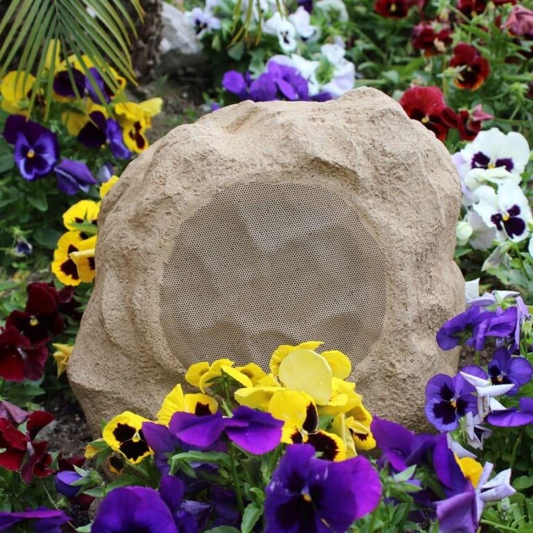 Tgd Audio Ors-602G 6.5″ Outdoor Rock Speaker (Granite) Rock-shaped outdoor speaker with circular perforated grille among colorful pansies.