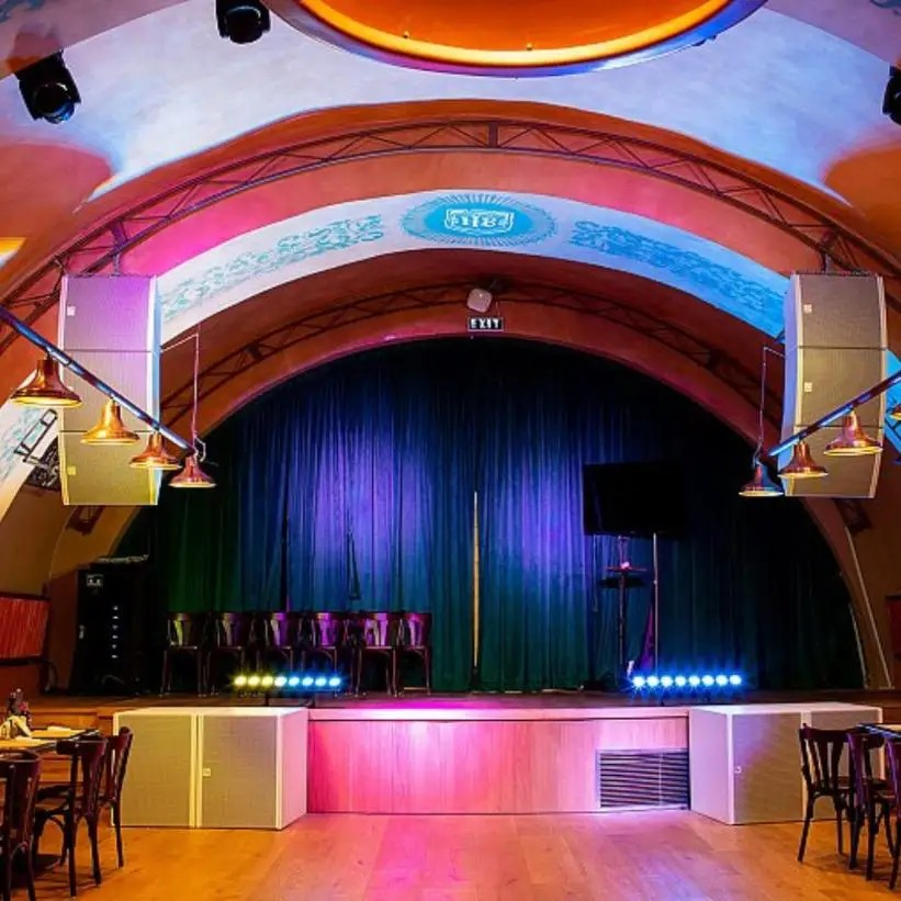 Electro-Voice Loudspeaker Line Array Passive 90° X 6° Indoor – 2X 8&Quot; Lf, 4X 1.25&Quot; Hf, Black Indoor event stage with green curtains, row of chairs, blue stage lights, and arched decorative ceiling in a colorful venue.