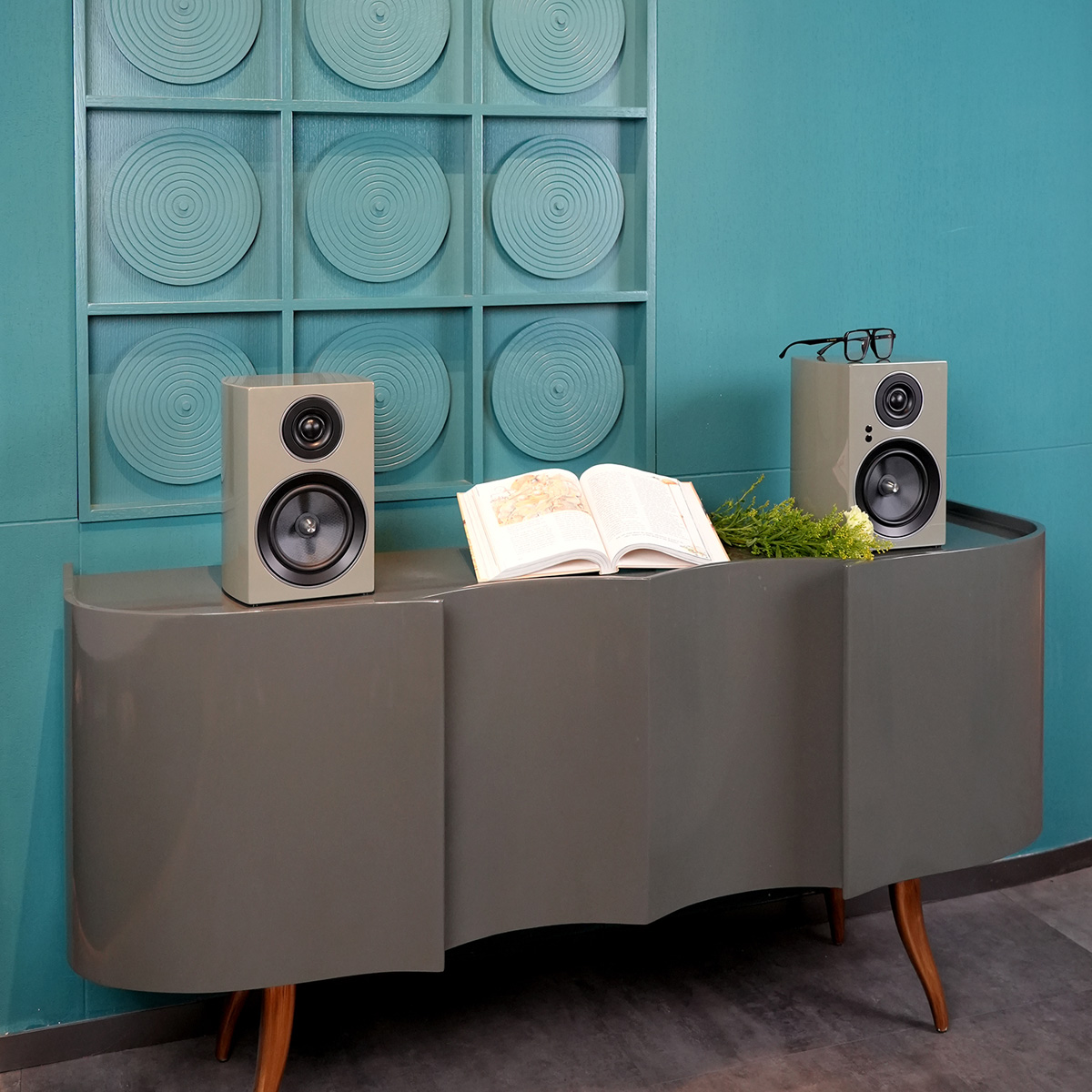 Jamo C707 Pa Active Bookshelf Speaker Pair of beige bookshelf speakers on a curved gray console.
