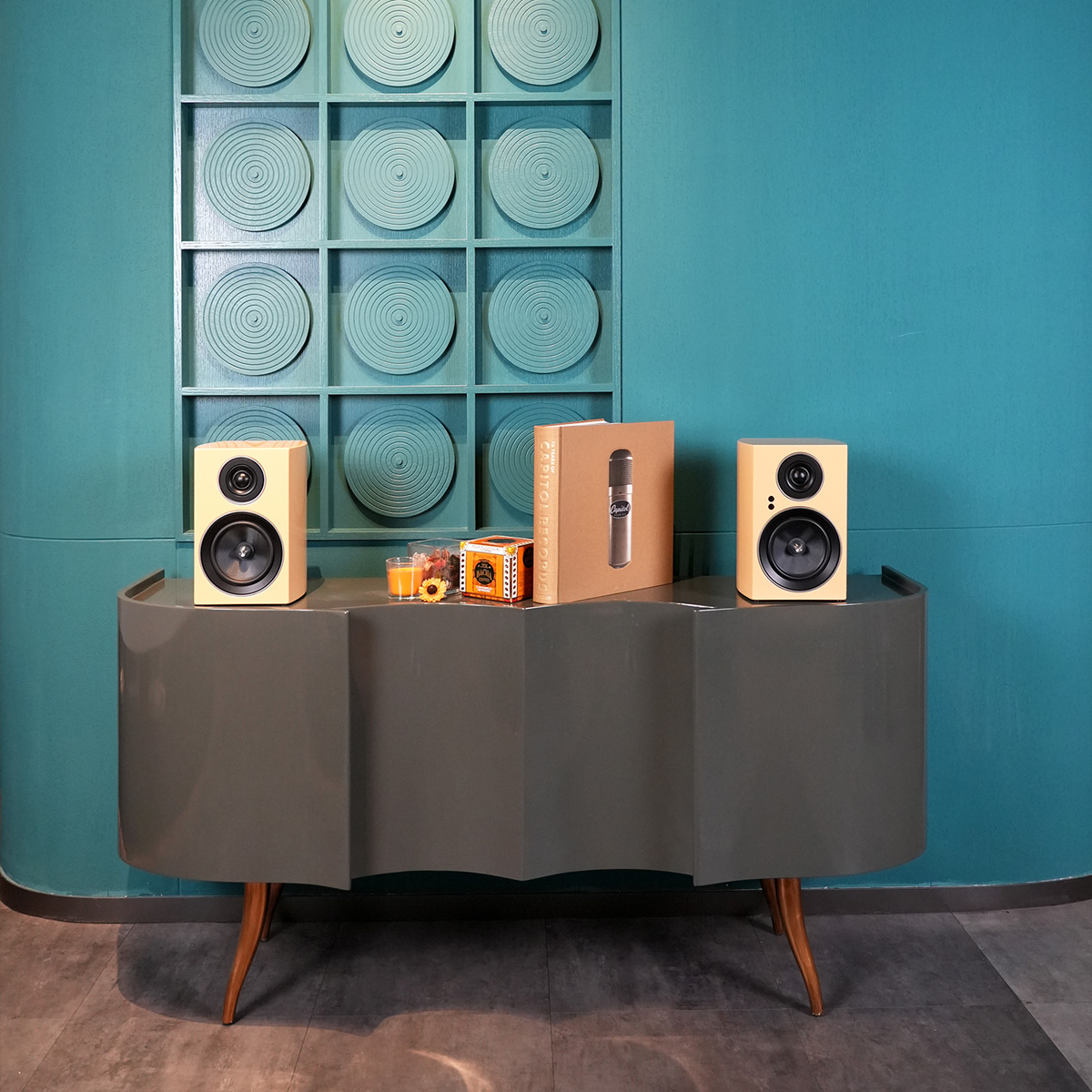 Jamo C707 Pa Active Bookshelf Speaker Two beige bookshelf speakers on curved console beside microphone box.